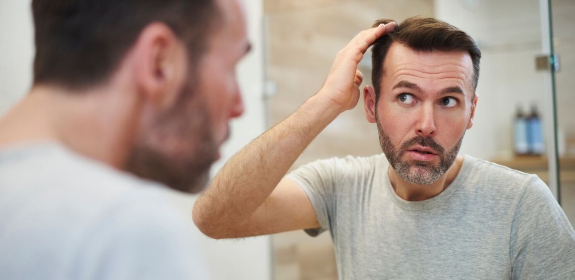 A man looking at his hair in the mirror.