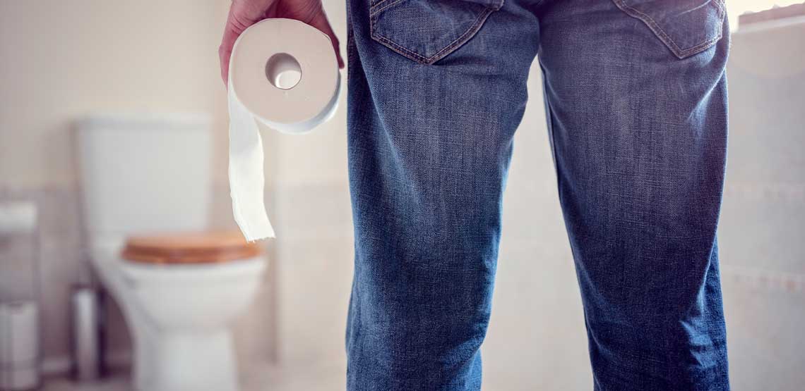 A person standing in front of a toilet, holding a toilet paper roll.