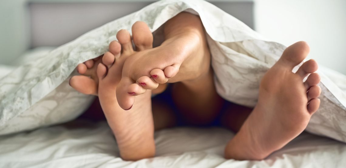 Feet of a man and a woman on top of each other, under a blanket