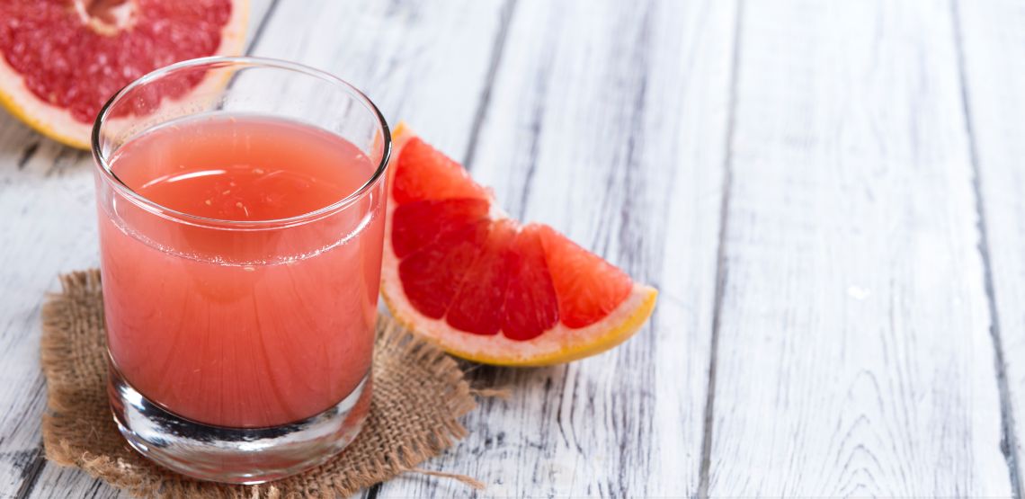 A glass of grapefruit juice with slices of pink grapefruit around it